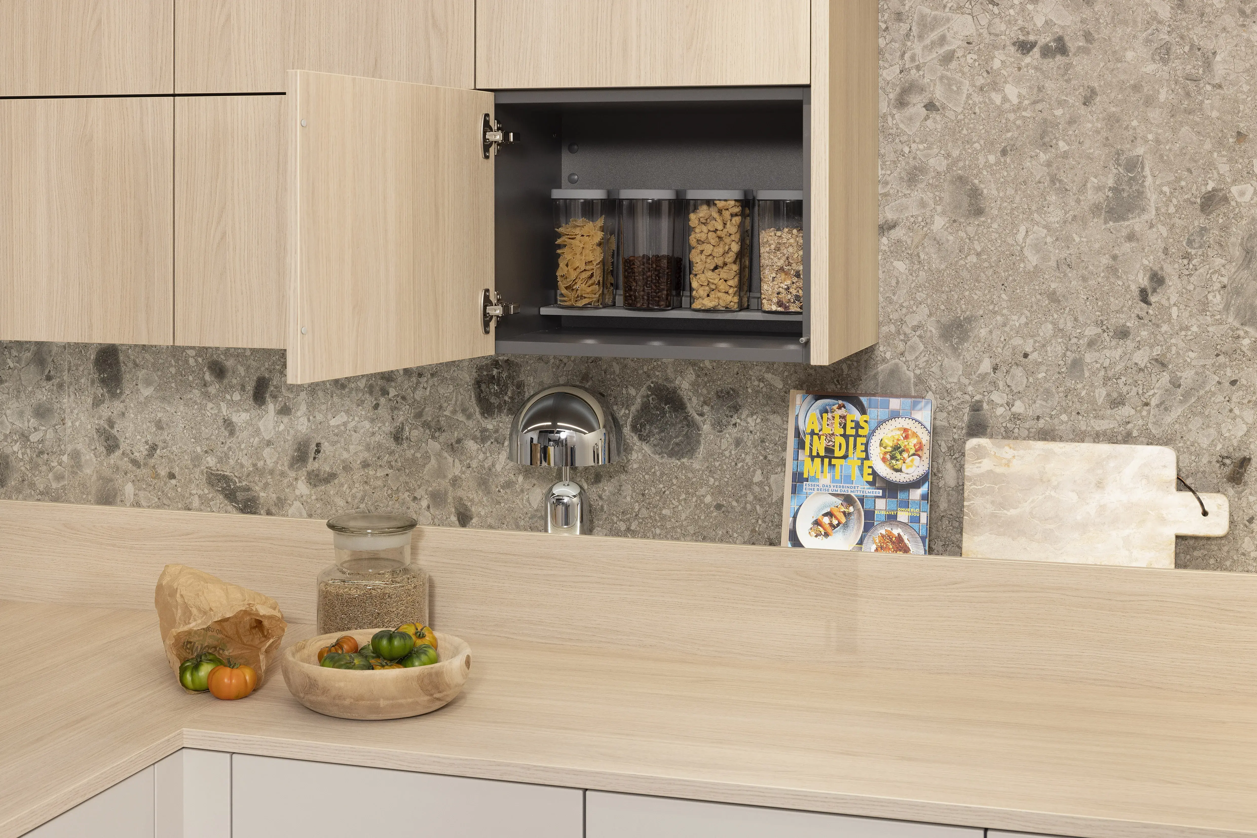 Moderne Küche mit offenem Schrank, Gewürzgläsern und frischem Gemüse auf der Arbeitsplatte. Steindekor in Nischenrückwand