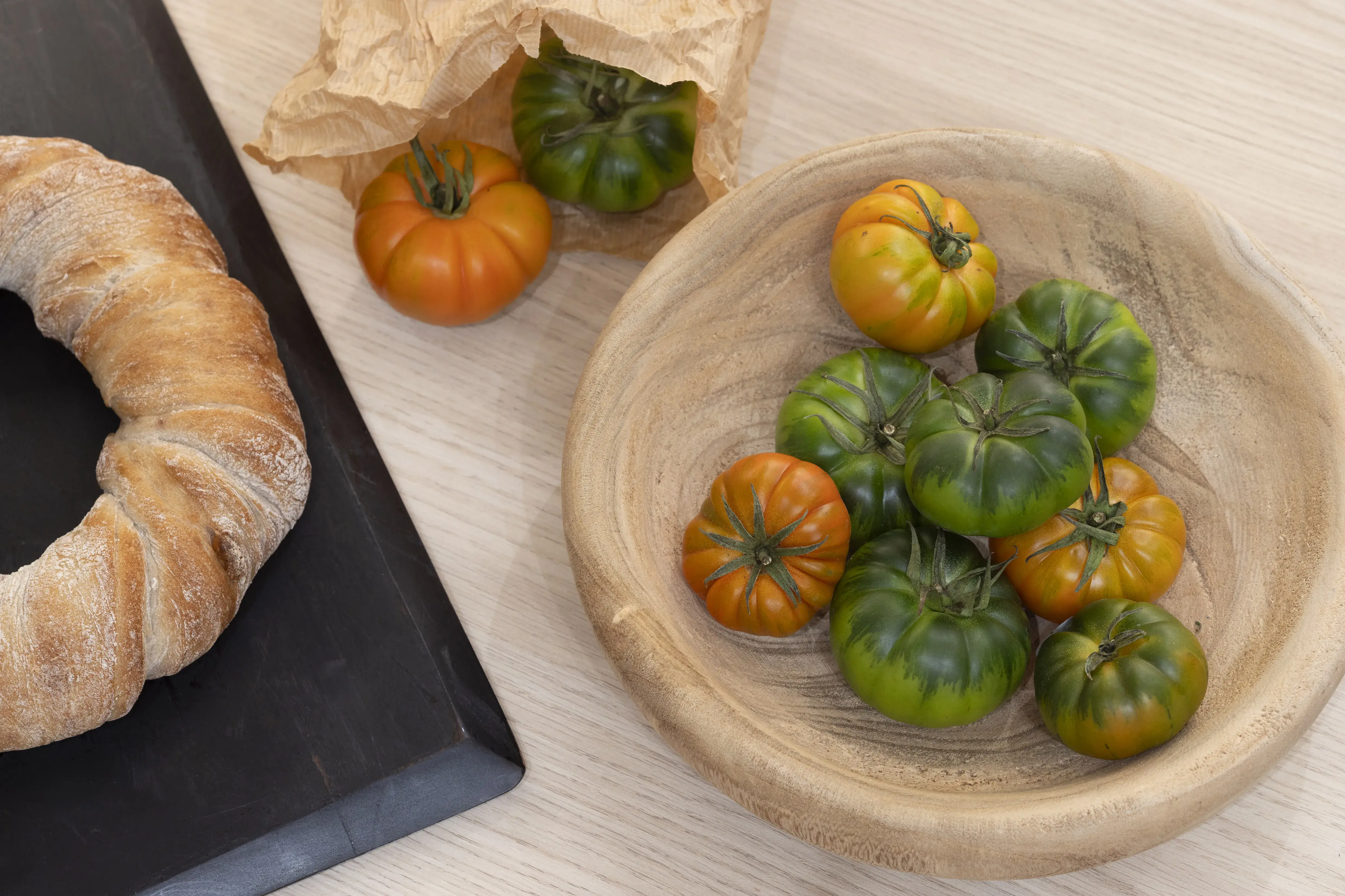 Grüne und orange Tomaten in einer Holzschale, daneben ein rundes Brot