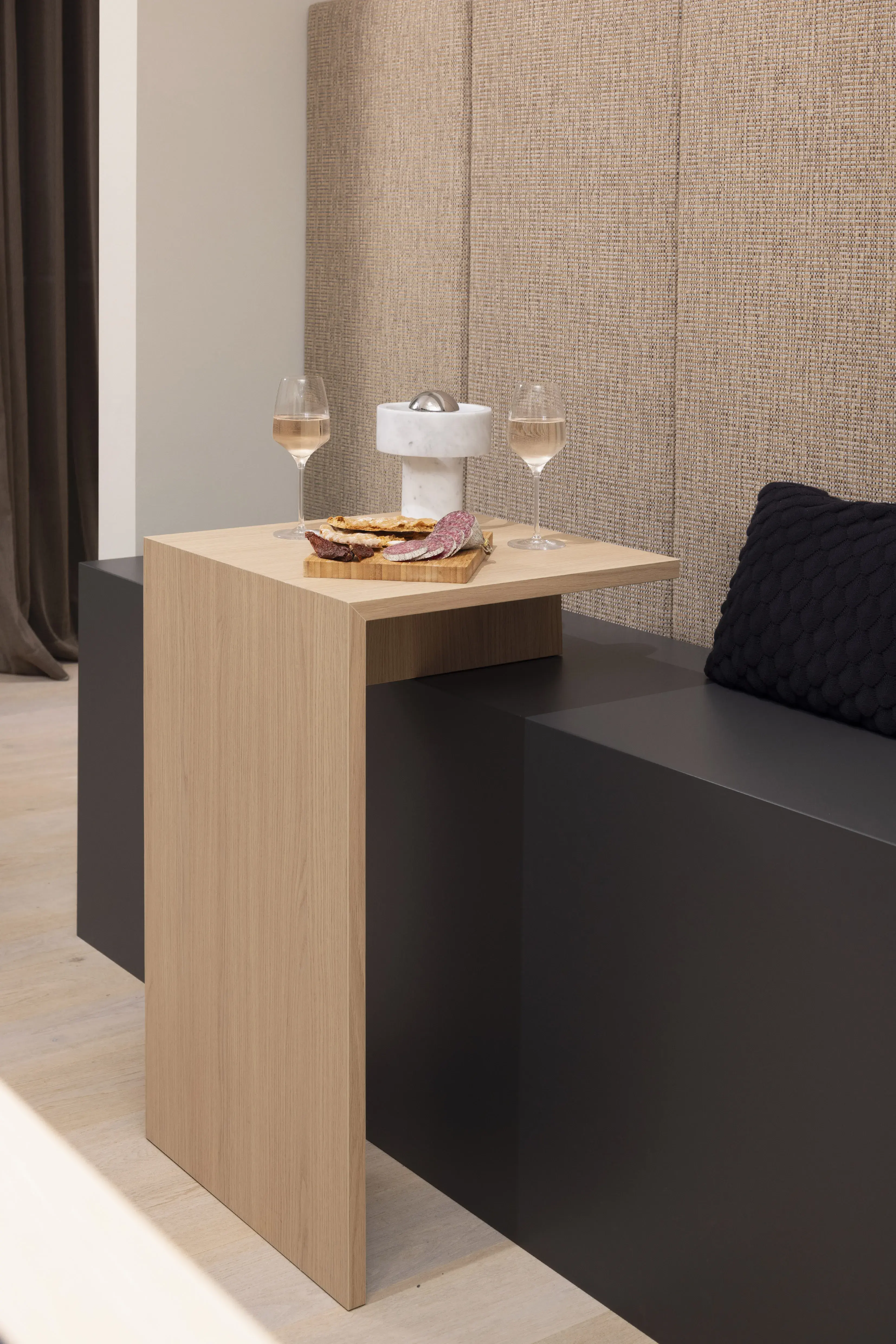 Kleiner Holztisch mit zwei Weingläsern, Snacks und schwarzem Kissen auf Sofa.