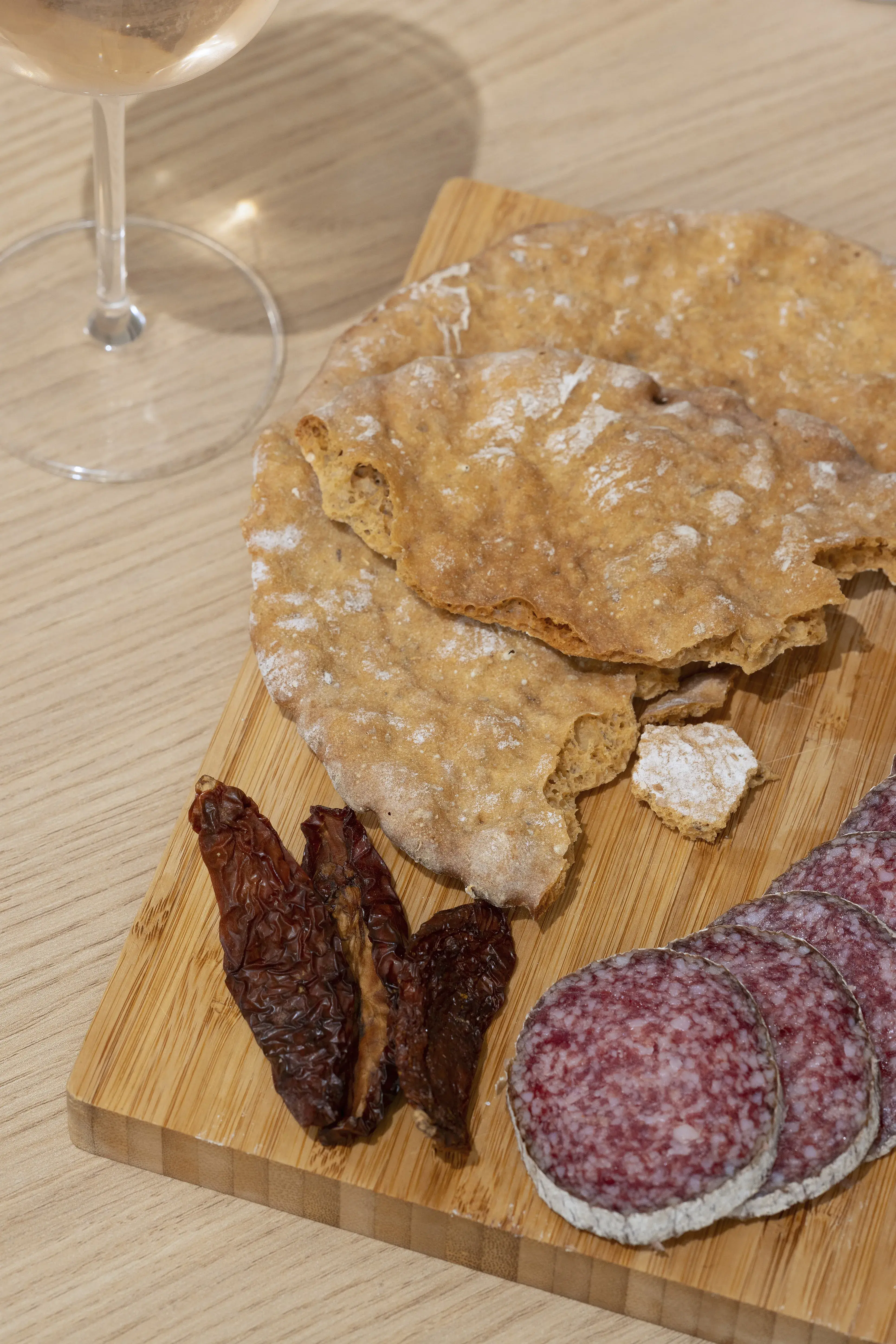 Brot, Salami, getrocknete Tomaten und ein Glas Wein auf Holzbrett.